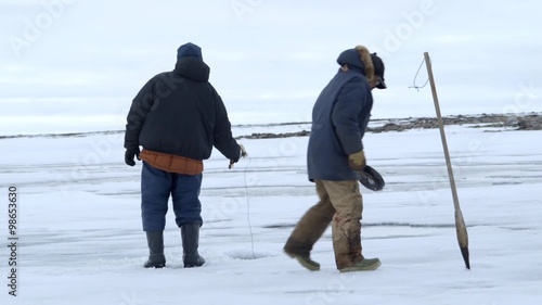 Pair of fisherman cut holes in ice during an arctic expedition.