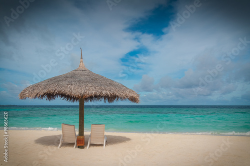 Straw parasol sunshade and sun loungers on a tropical beach in the Maldives