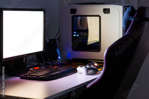 Custom built desktop computer for gaming on the table with joystick, monitor, keyboard, chair under low light. Selective focus.