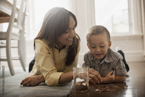 A woman and a child lying on the floor, playing with brass and silver coins, putting them into a glass jar.  photo
