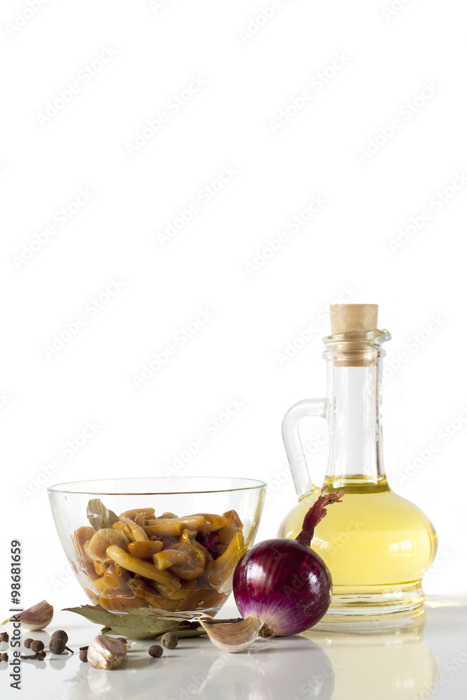 Olive oil and delicious marinated mushrooms in glass bowl, red onion, garlic and spices on white background Olive oil and delicious marinated mushrooms in glass bowl, red onion, garlic and spices on white background