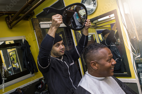 Barber shows short haircut with mirror to happy client in a barber shop.
