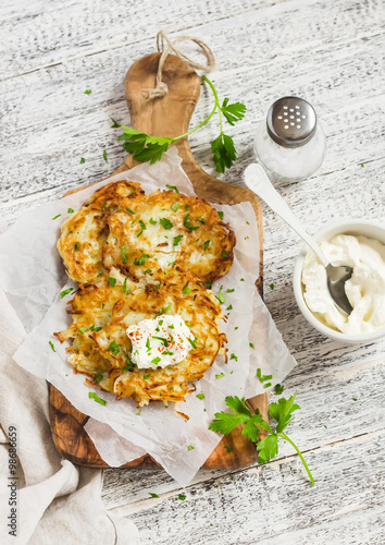 Potato pancakes or latkes with cream served on olive cutting Board over white wooden table. Rustic style. Healthy food