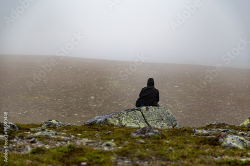 Man sitting alone on a large stone  back against camera