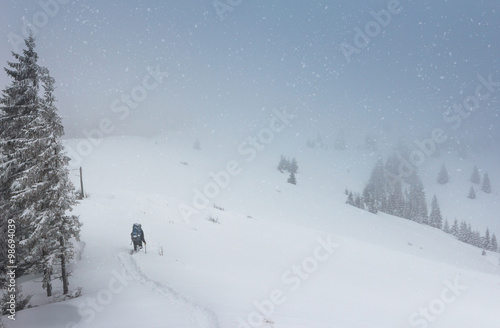 Tourists with backpacks climb to the top of the mountain in fog and snow fall.