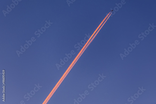 Foto Airplane with contrail high in the sky at sunset