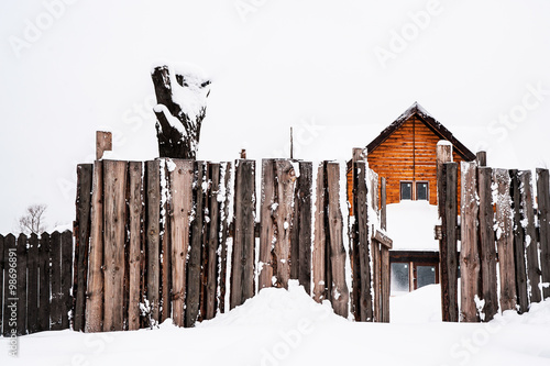 Wooden Cabine and Fence under snow. Wooden cottage in the russian village and wooden fence under the thick layer of white snow in minimalsitic style. photo