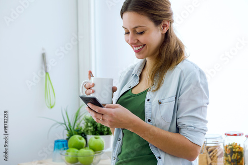 Beautiful young woman using her mobile phone and enjoying breakf