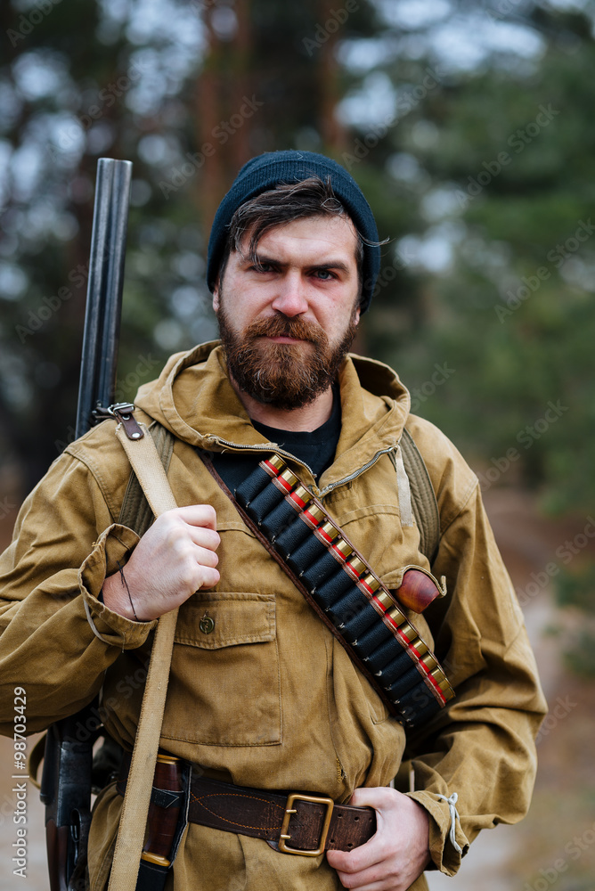 brutal hunter, bearded man in warm hat with a gun in his hand, a knife