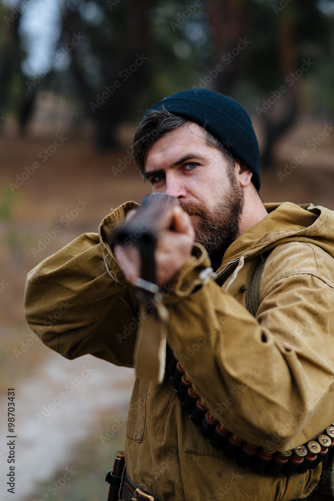 brutal hunter, bearded man in warm hat with a gun in his hand, a knife a backpack and smoking pipe in the wild forest in the autumn brutal hunter, bearded man in warm hat with a gun in his hand, a knife a backpack and smoking pipe in the wild forest in the autumn