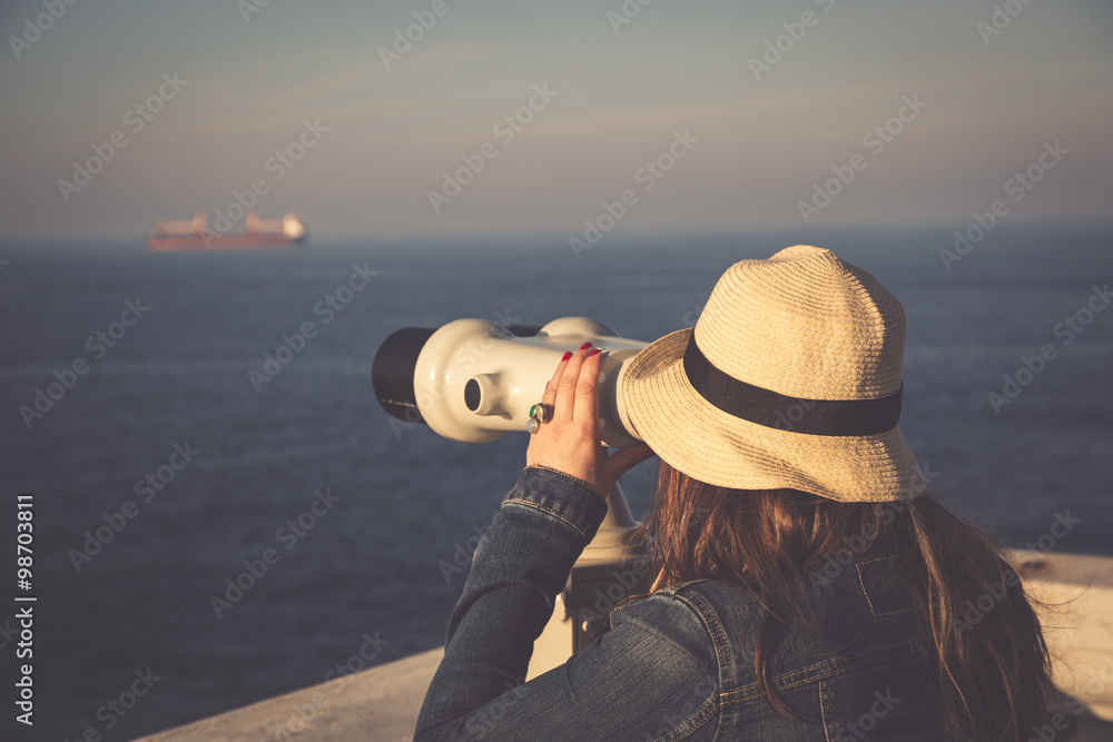 Young girl looking through a coin operated binoculars on the sea