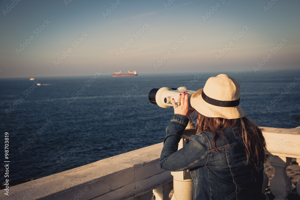 Young girl looking through a coin operated binoculars on the sea