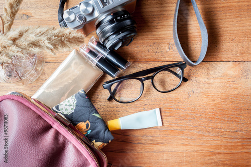 Camera, eyeglass, powder, lipstick and bag on a wood background