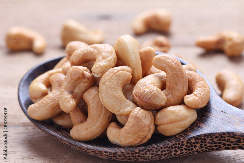 Cashew nuts in wooden ladle on wooden background