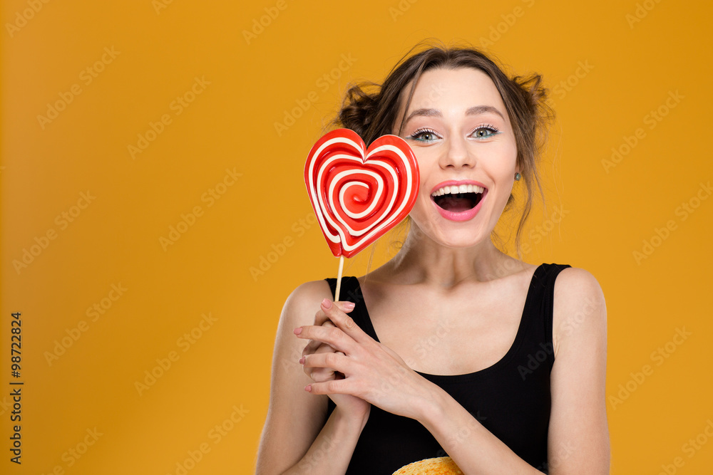 Joyful charming young woman holding bright heart shaped candy Joyful charming young woman holding bright heart shaped candy