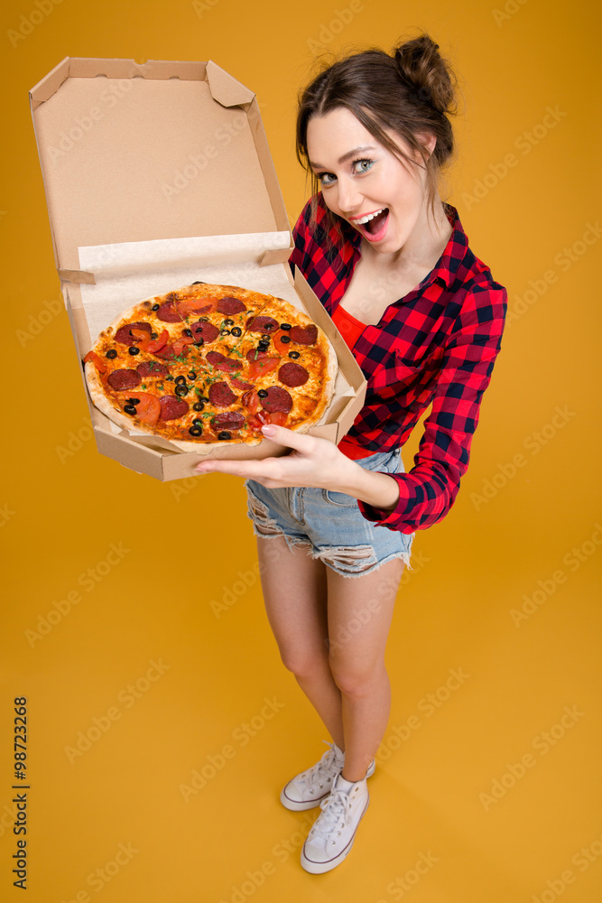 Beautiful smiling young woman standing and showing pizza