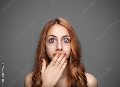 Girl covering her mouth with hand, isolated on gray.