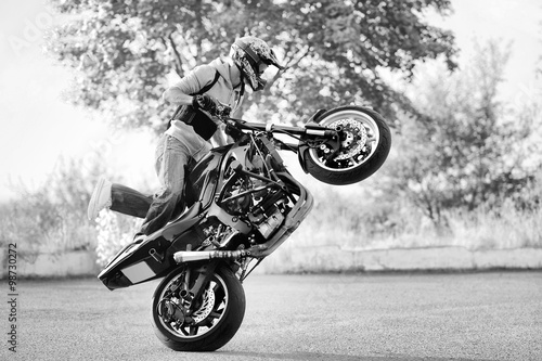 Extreme racer. Black and white soft smudged focus portrait of a man wearing protection gear and helmet standing on a motorcycle