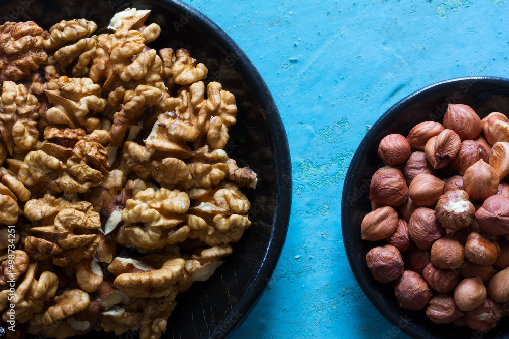 Part of the round wooden plates with the cleared walnuts and hazelnuts on a blue background. Part of the round wooden plates with the cleared walnuts and hazelnuts on a blue background.