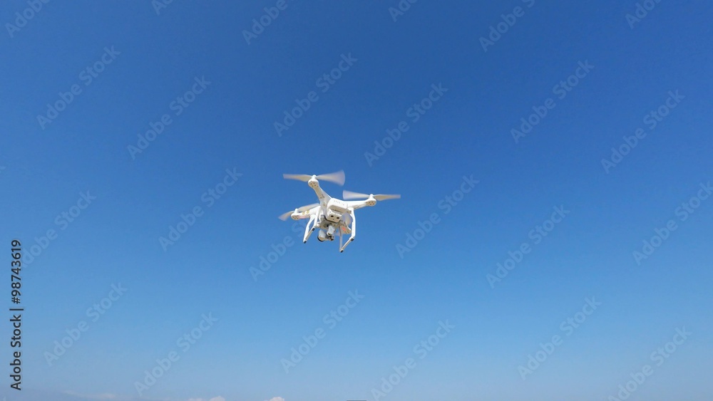 White remote controlled drone equipped with high resolution video camera hovering in mid air White remote controlled drone equipped with high resolution video camera hovering in mid air