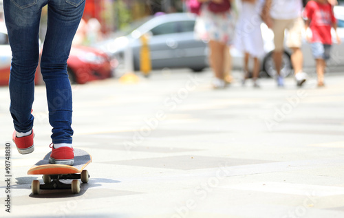 young skateboarder legs riding on skateboard on city