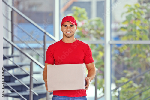 Konstfotografi Delivery concept - postman in red uniform holding package near stairs