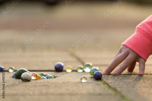 Child playing with marbles on yhe sidewalk.
old-fashioned toys still in use today.