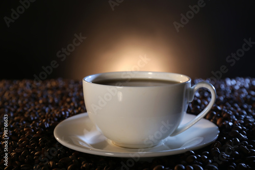 Cup of hot coffee among coffee beans on dark background