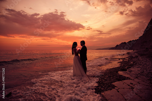 A just married couple staying at the beach. Romantic wedding sunset. Splashing ocean waves and beautiful sky