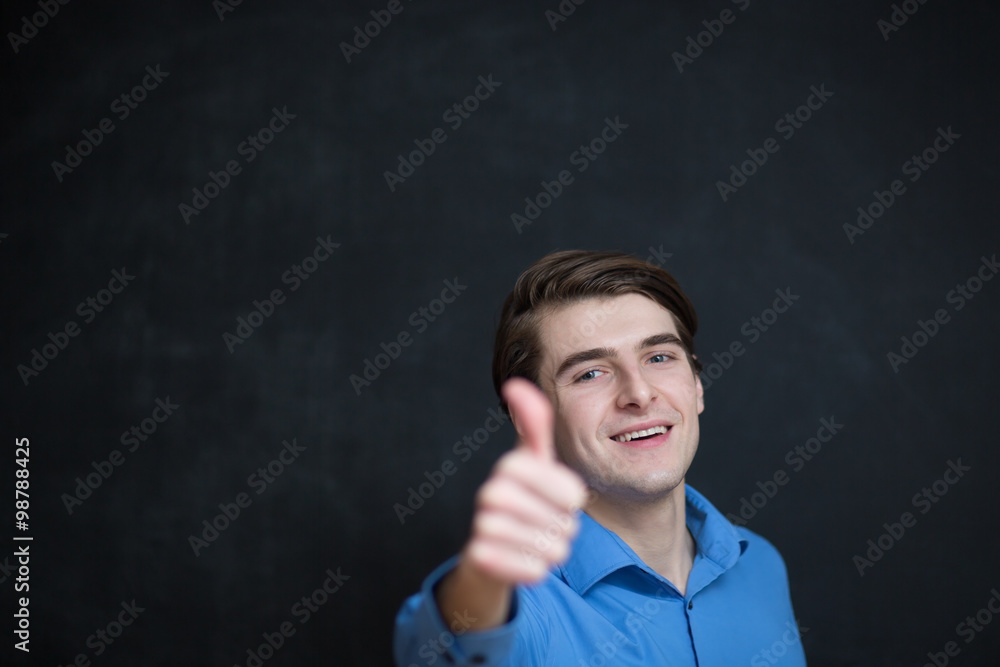 Happy young man is smiling and showing thumbs up. Dark backgroun