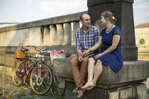 Couple with bicycles sitting on a stone embankment.