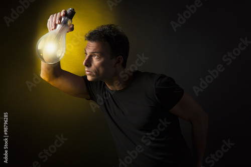 Concetto di pensiero ed immaginazione: uomo tiene tra le mani una lampadina accesa. Sfondo nero photo