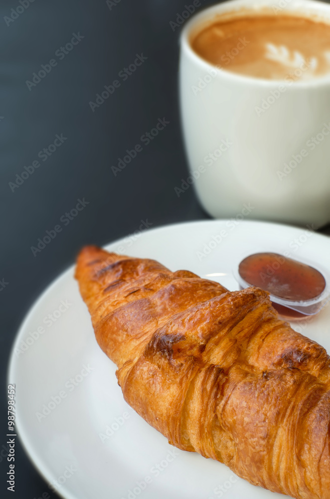 butter croissant and hot latte on black background