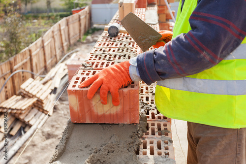 Foto Construction mason worker bricklayer installing red brick with trowel putty knif