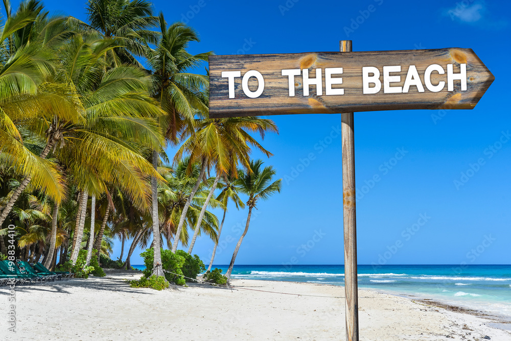 Beach Wood Sign with text To The Beach, Palm Trees, Tropical See and Blue Sky