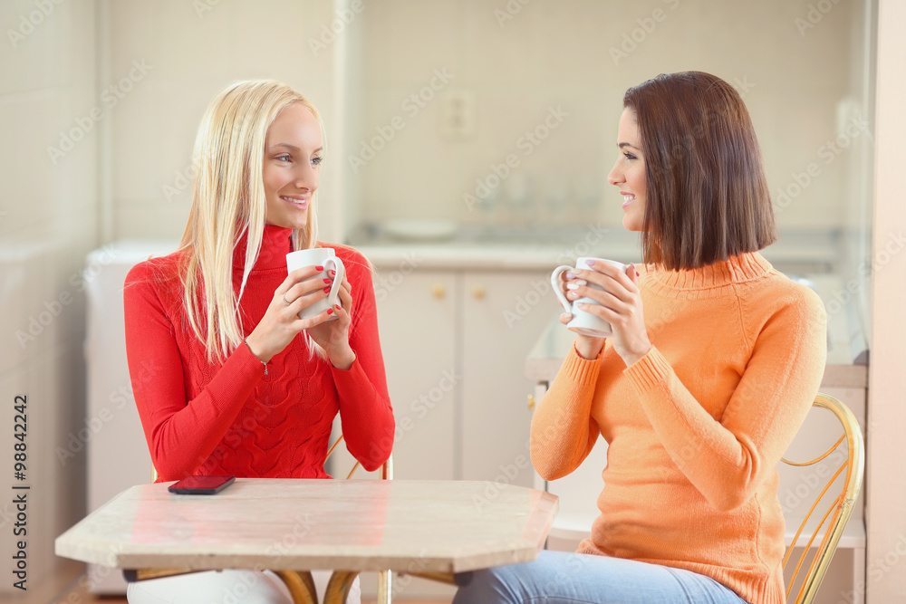 Two young girlfriends having a cup of coffee at home