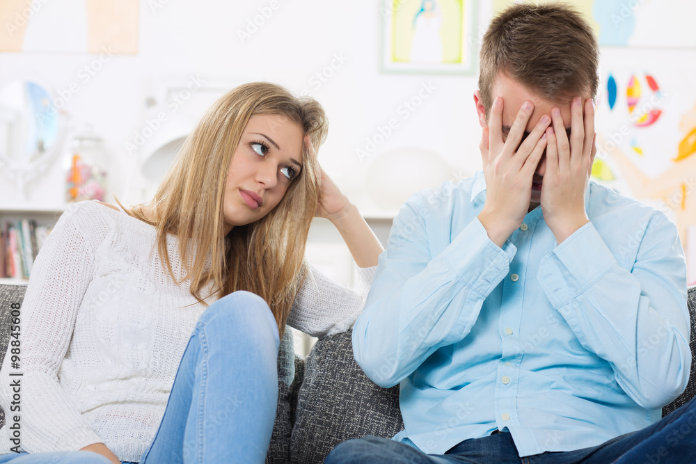 Young couple arguing on the sofa, man holding his head in his hands Young couple arguing on the sofa, man holding his head in his hands
