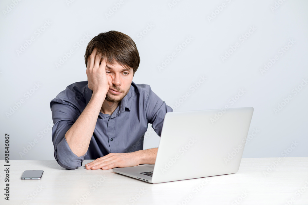 Feeling sick and tired. Frustrated young man holding head in hands and looking at laptop while working late at his working place Feeling sick and tired. Frustrated young man holding head in hands and looking at laptop while working late at his working place