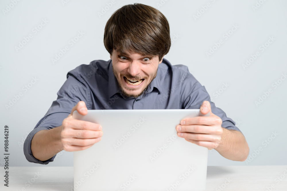 Feeling sick and tired. Frustrated young man holding head in hands and looking at laptop while working late at his working place Feeling sick and tired. Frustrated young man holding head in hands and looking at laptop while working late at his working place