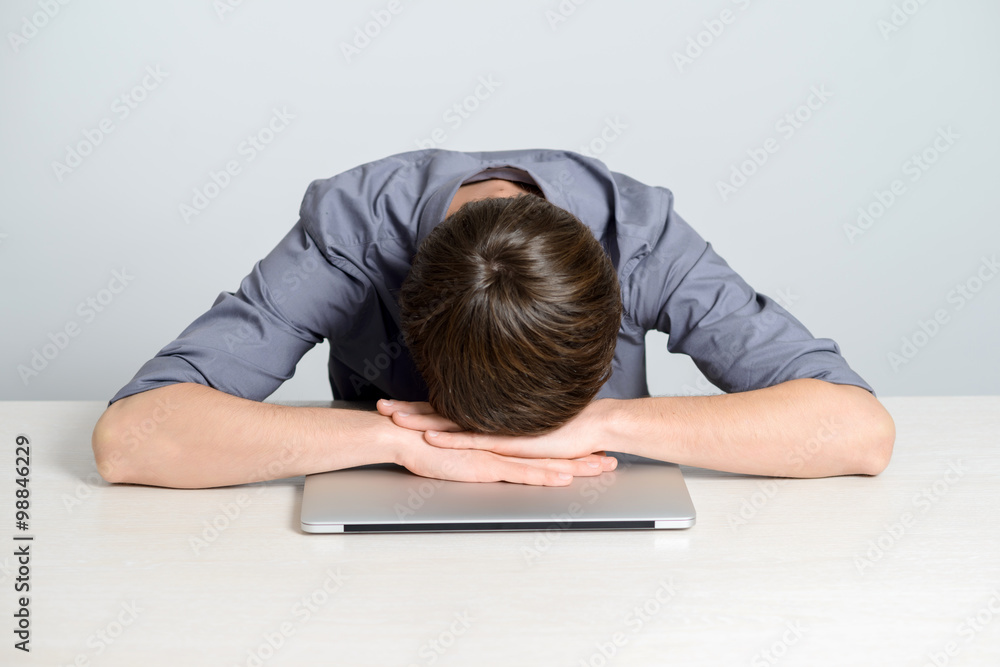 Feeling sick and tired. Frustrated young man holding head in hands and looking at laptop while working late at his working place Feeling sick and tired. Frustrated young man holding head in hands and looking at laptop while working late at his working place