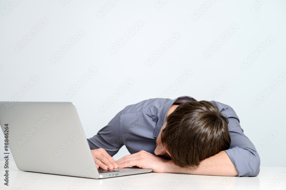 Feeling sick and tired. Frustrated young man holding head in hands and looking at laptop while working late at his working place Feeling sick and tired. Frustrated young man holding head in hands and looking at laptop while working late at his working place