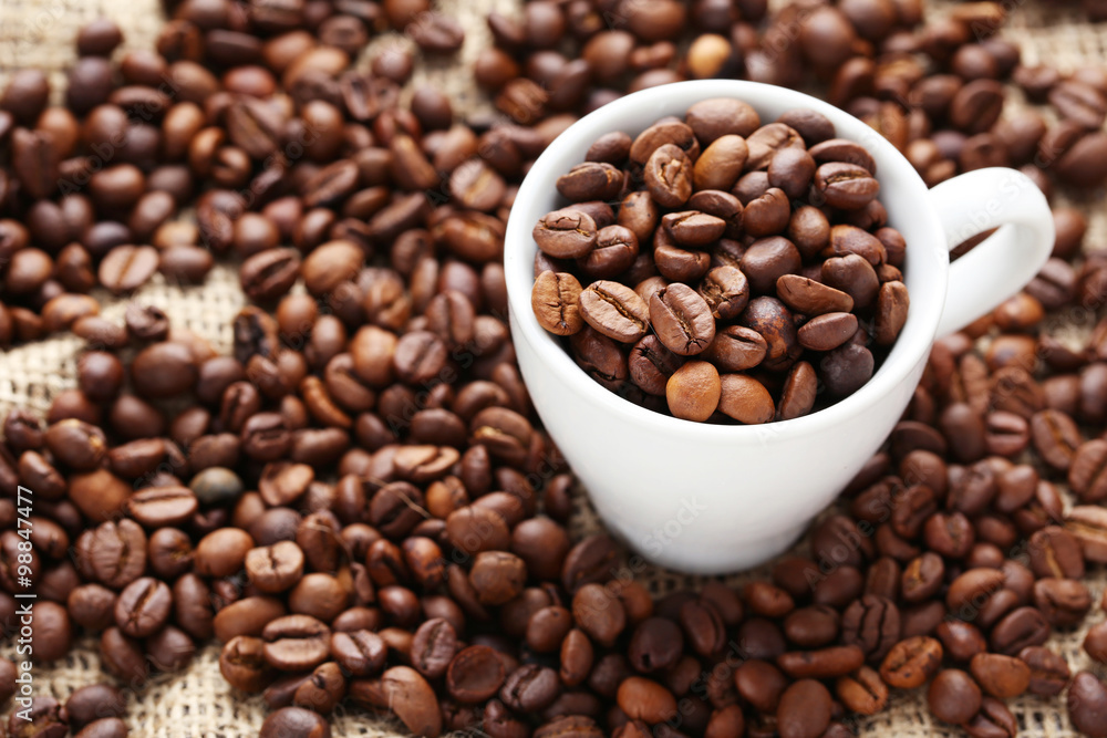 Coffee beans in cup on a sack, close up