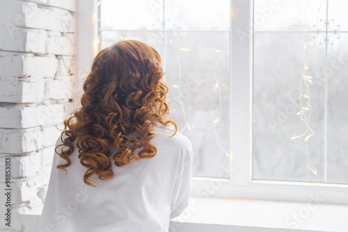 Young woman looking in window in loft apartment.  rear view. White bedroom interior, women's loneliness,
