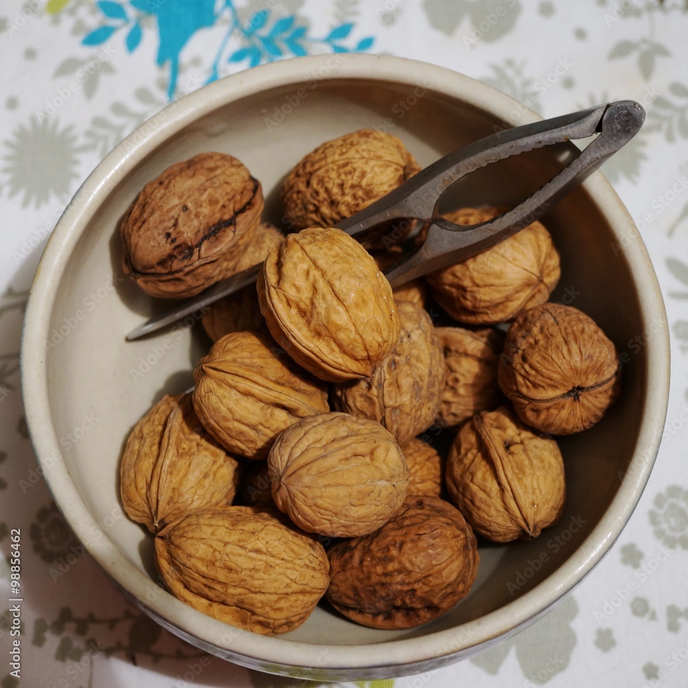 Bowl of fresh walnuts in the shell with a nutcracker Bowl of fresh walnuts in the shell with a nutcracker