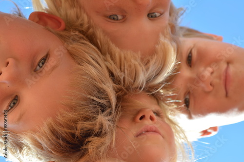 Three little boys and a girl looking at the camera against the blue sky.
