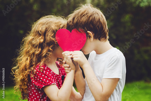 Cute children holding red heart shape in summer park. Valentines