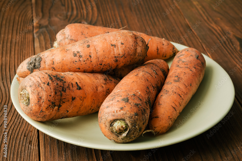 Unpeeled carrots in a green plate on a brown wooden table, close Unpeeled carrots in a green plate on a brown wooden table, close