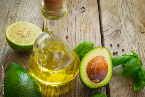 Vegetable oil, avocado, lime and basil on old wooden background