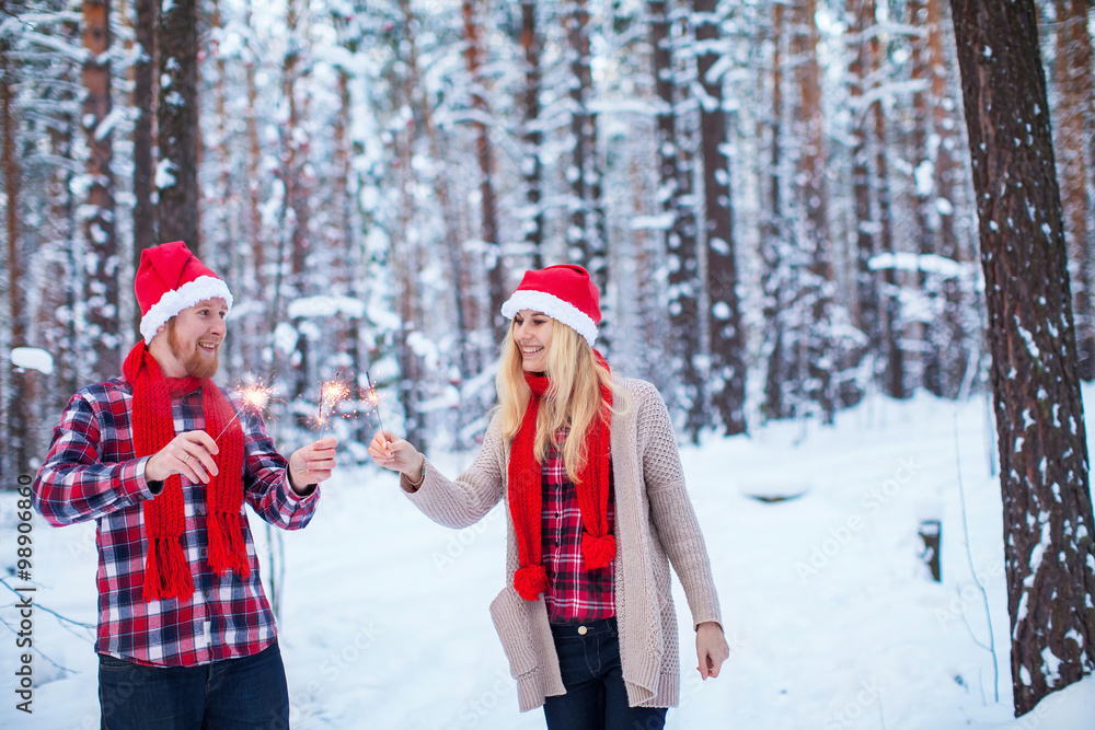 young couple in Christmas hats with sparklers in the winter forest