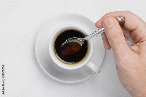 Male hand stir slowly black coffee with spoon in coffee cup against white background with place for text top view